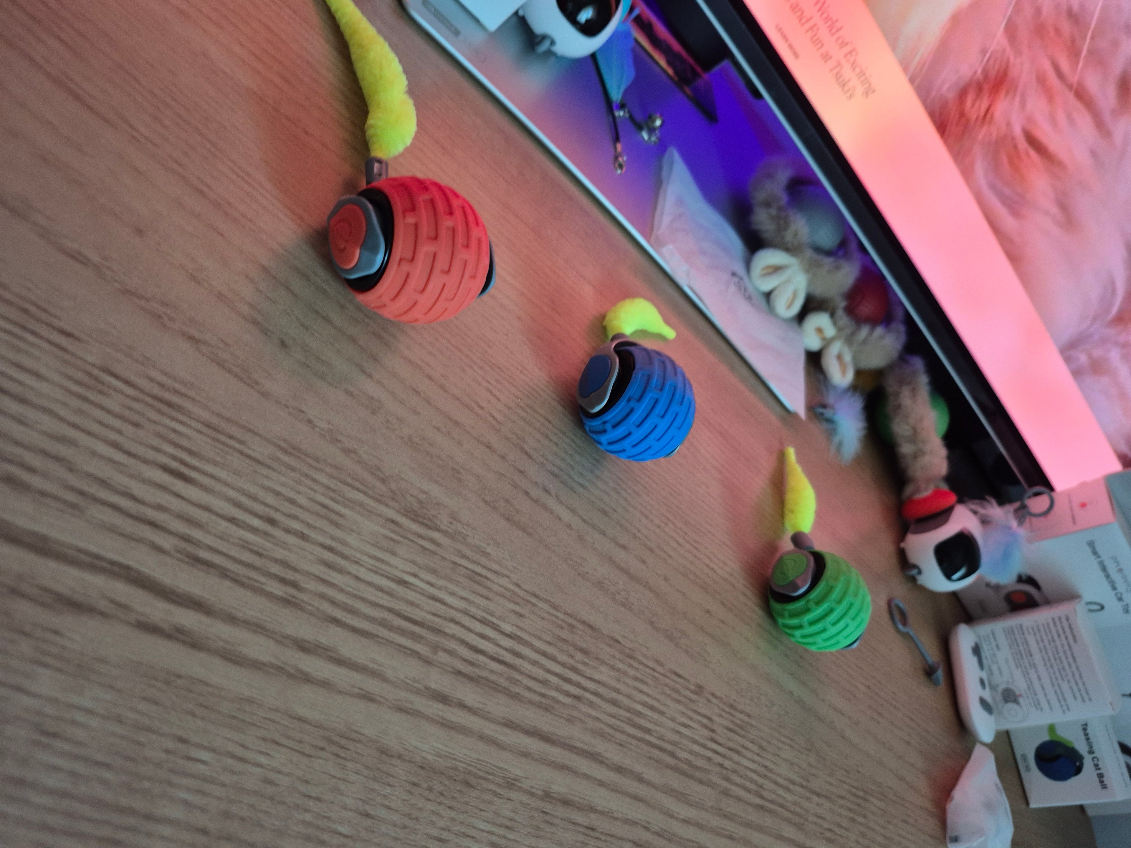 Colorful dog toys hanging on a wooden board with a TV screen in the background.